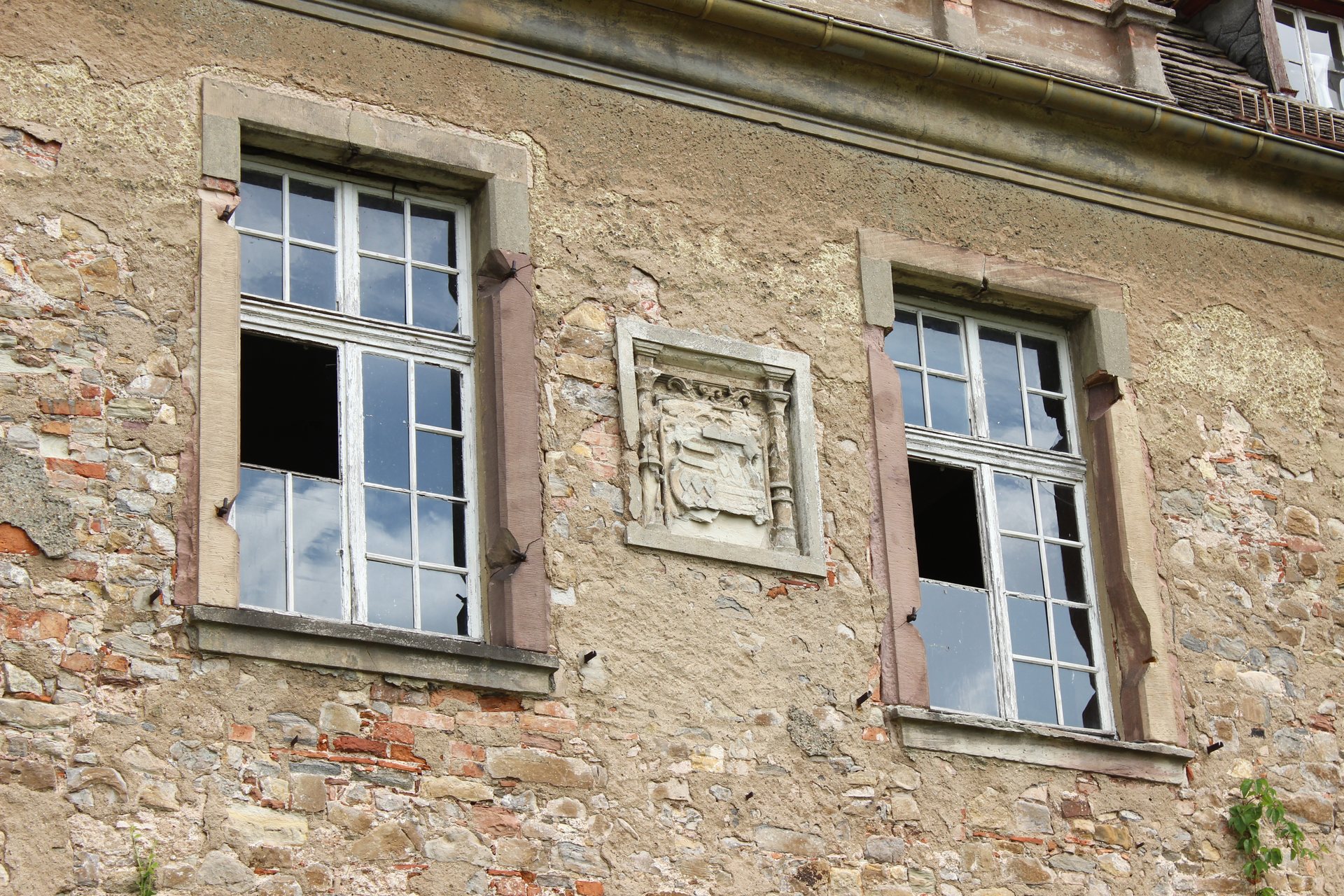 Fassade von Schloss Seeburg mit zerbrochenen Fenstern und historischem Wappenrelief